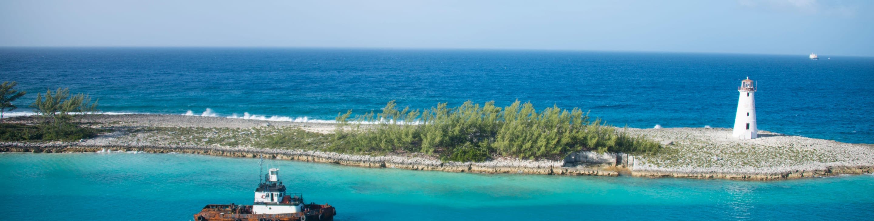 An aerial view of a curving beach where pink-white sand, turquoise lagoons and green coastal vegetation meet the open sea in the Bahamas