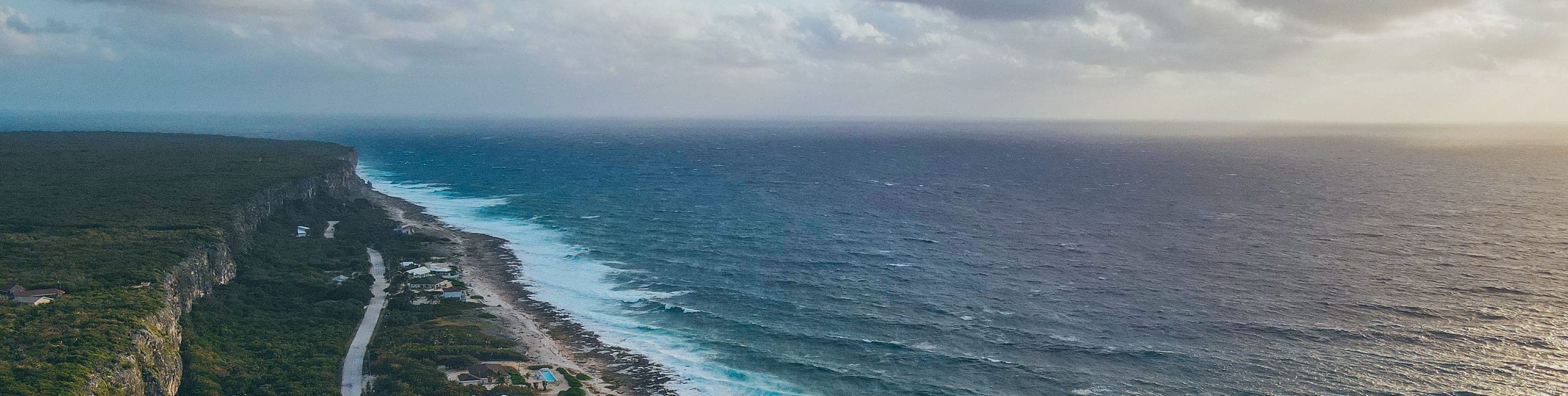 A turquoise cove with clear water lapping a white sand beach, dark rocky outcrops in the background and a green sea-grape leaf in the foreground